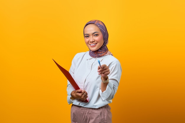 Mooie Aziatische vrouw die mappen vasthoudt en met een pen wijst en naar de camera kijkt met een lachend gezicht