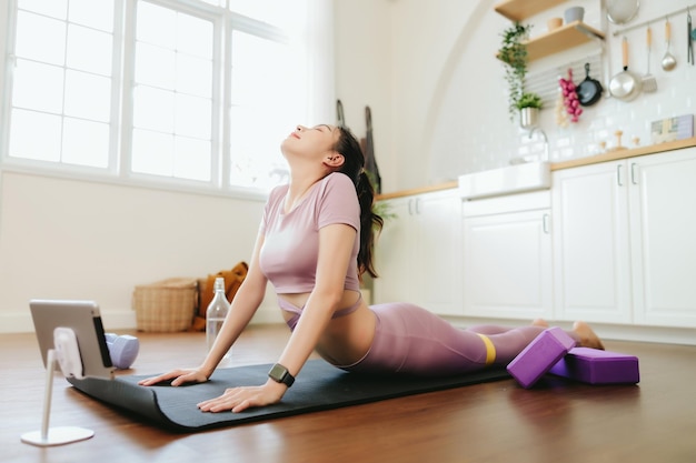 Mooie Aziatische vrouw die thuis sportkleding draagt, terwijl ze naar een tutorial op tablet kijkt