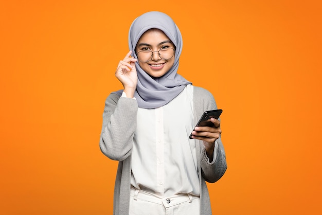 Mooie aziatische vrouw die vrolijk een smartphone op oranje muur houdt