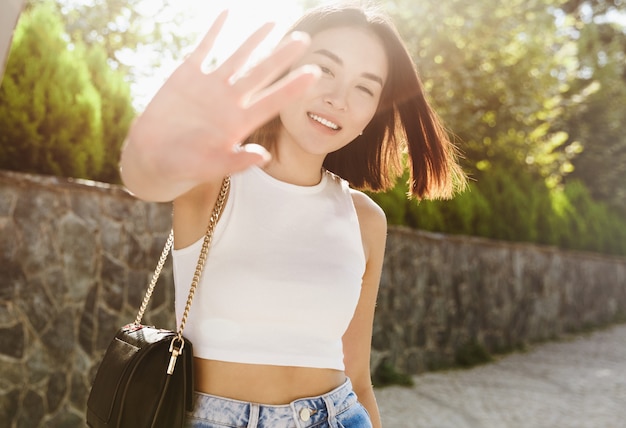 Mooie Aziatische vrouw die zichzelf bedekt van camera en glimlachen, poseren in trendy outfit, wandelen in het park