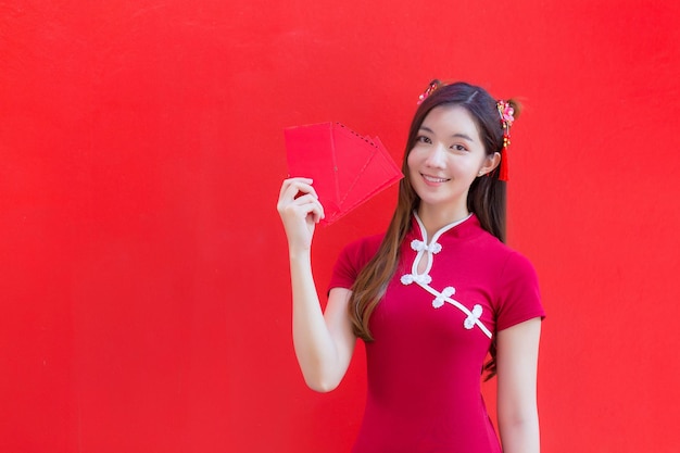 Mooie Aziatische vrouw draagt een rode cheongsam en houdt rode enveloppen vast terwijl ze lacht met een rode achtergrond