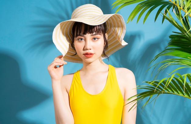 Mooie Aziatische vrouw, gekleed in gele jumpsuit op blauw met palmbladeren