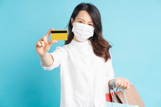 Mooie Aziatische vrouw, gekleed in wit masker met boodschappentassen en bankkaart in de hand