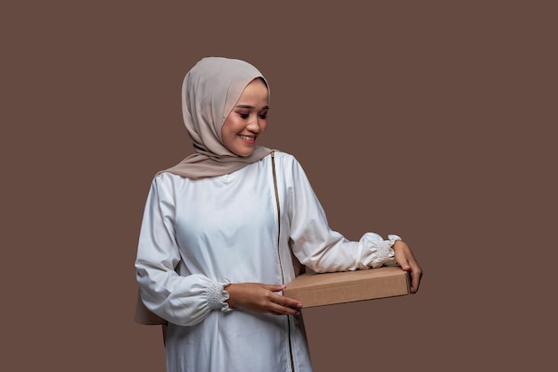Mooie aziatische vrouw in hijab die pizzadoos met beide handen vasthoudt terwijl ze glimlacht
