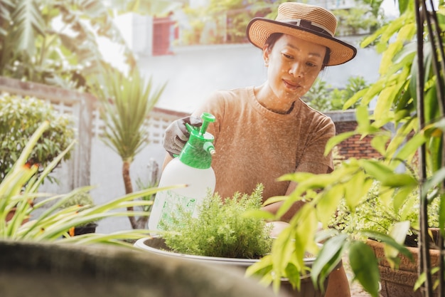 Mooie aziatische vrouw in hoed die plant water geeft door mistige spuitfles in de tuin