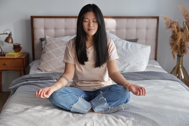 Mooie aziatische vrouw in vrijetijdskleding die yogales beoefent, ademhalingsmeditatie op het bed