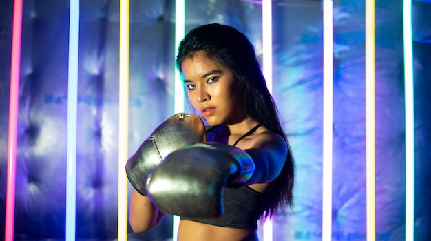 Mooie aziatische vrouw is trainen en stoten met zilver gouden wanten handschoenen. office girl-oefeningen in moderne kleur neon muay thai boxing gym met zweetwaterplons