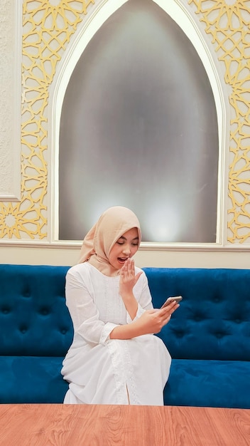 Foto mooie aziatische vrouw met een hijab openhartige uitdrukking van verrassing controleert haar mobiele telefoon gadget s