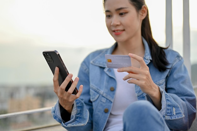 Mooie Aziatische vrouw met een smartphone en een creditcard mobiel bankieren geld overmaken