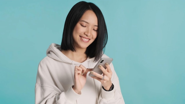 Mooie Aziatische vrouw met een witte hoodie aan het chatten met vriendjes die er gelukkig uitzien, geïsoleerd op een blauwe achtergrond