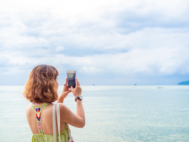 Mooie aziatische vrouw met kort haar die een smartphone gebruikt, neem een foto van het zeegezicht