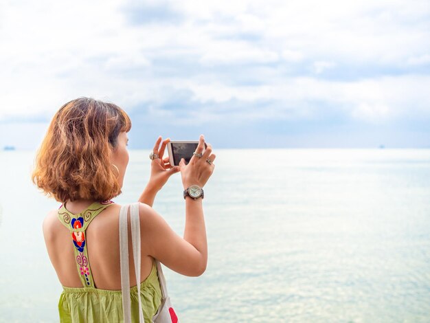 Mooie aziatische vrouw met kort haar die een smartphone gebruikt, neem een foto van het zeegezicht