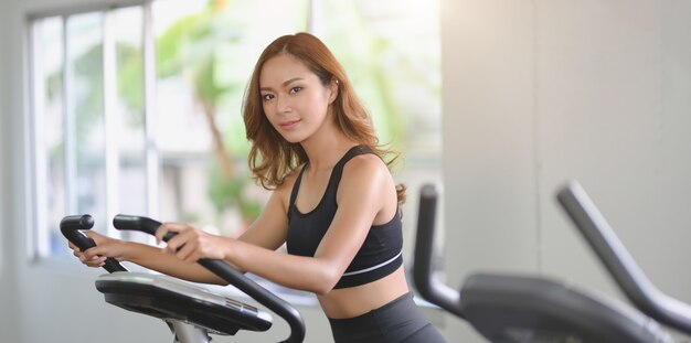 Mooie Aziatische vrouw met slank lichaam die cardiotraining op elliptische machine doen