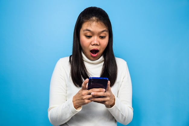 Mooie Aziatische vrouw met witte T-shirt met blauwe geïsoleerde achtergrond vrouwen kijken naar smartphone