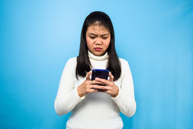 Mooie Aziatische vrouw met witte T-shirt met blauwe geïsoleerde achtergrond vrouwen kijken naar smartphone