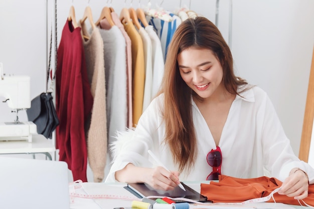 Mooie aziatische vrouw modeontwerper zitten in de kledingwinkel en studio. voor de laptop om online te vergaderen. zakelijke online influencer op social media concept.