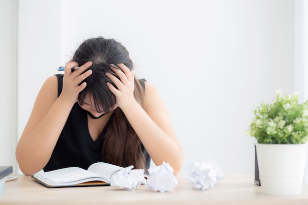 Mooie Aziatische vrouw moe en gestrest met schrijven overwerkt bij bureau