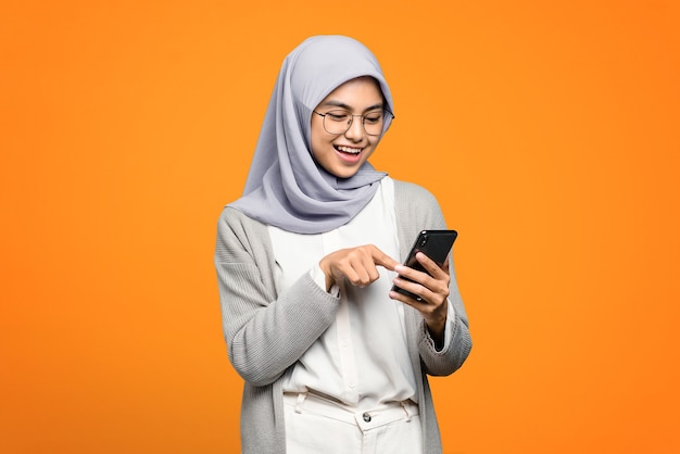 Mooie Aziatische vrouw vrolijk met behulp van een smartphone op oranje muur