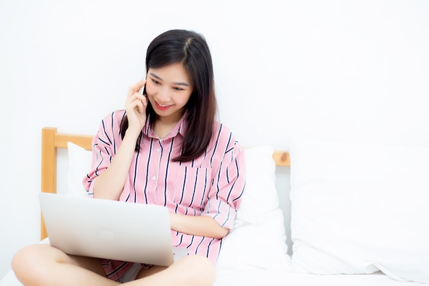 Mooie aziatische vrouw zittend op bed met behulp van laptopcomputer