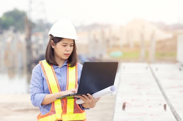 Mooie Aziatische vrouwelijke ingenieur in witte veiligheid harde hoed met behulp van laptop computer notebook doet werk op de bouwplaats buiten kantoor. Idee voor moderne werkende vrouw.