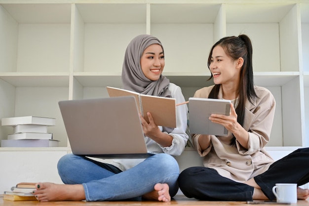 Mooie Aziatische vrouwelijke student in de bibliotheek met haar moslimvriend die het project bespreekt