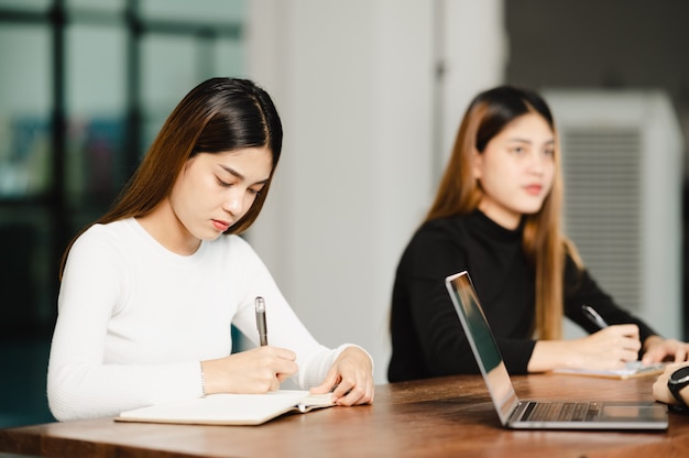 Mooie aziatische vrouwelijke student zit voor examen aan universiteitsklasstudenten die in de rij onderwijslevensstijl hogeschool zitten