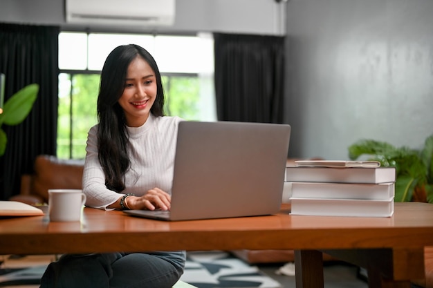 Mooie Aziatische vrouwelijke werkende browse-website met behulp van laptopcomputer in haar woonkamer