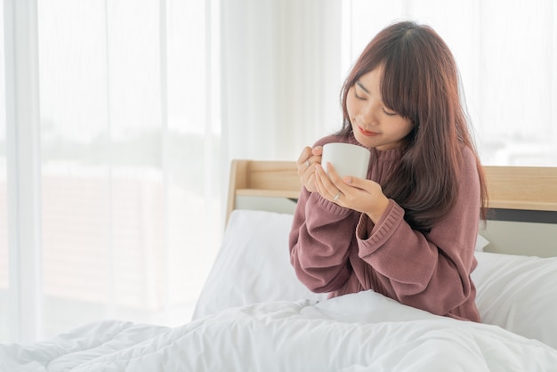 mooie Aziatische vrouwen die 's ochtends koffie op bed drinken