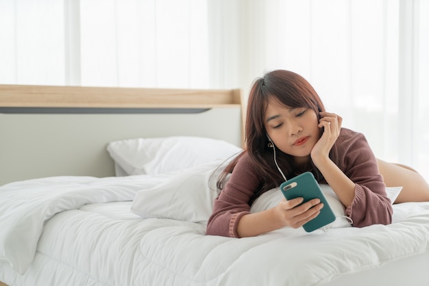 mooie Aziatische vrouwen die smartphone op bed spelen