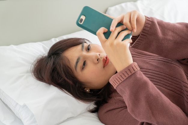 mooie Aziatische vrouwen die smartphone op bed spelen