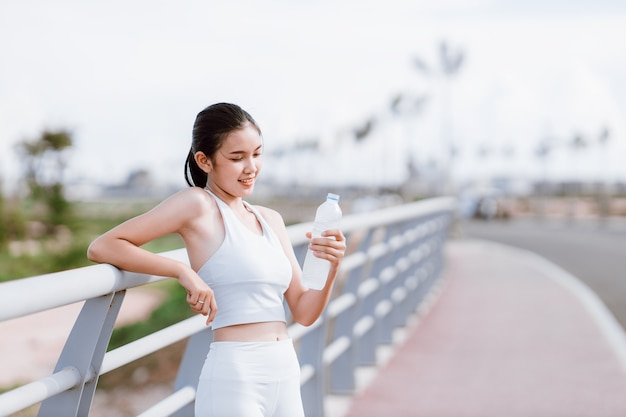 Mooie Aziatische vrouwen in sportkleding die buiten staan met een waterfles om te drinken na het sporten. Gezond vrouwenconcept. Hardlopen training.