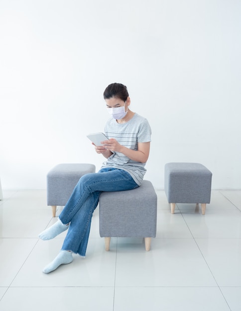 Foto mooie aziatische vrouwen werken thuis met behulp van tablet, comfortabel zittend op de bank, tijdens quarantaine in pandemie van coronavirus. werken vanuit huis en sociaal afstandsconcept.