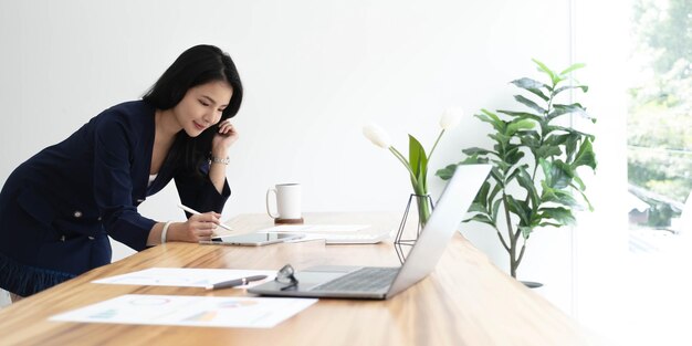 Mooie Aziatische zakenvrouw analyseert grafieken met behulp van laptop rekenmachine op kantoor
