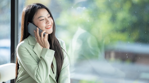 Mooie aziatische zakenvrouw glimlach en het gebruik van smartphone werken Glimlach mooie aziatische zakenvrouw met pak werkend kantoor met behulp van smartphonephone Gelukkige aziatische zakenvrouw die mobiele telefoon gebruikt