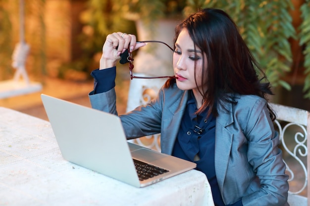 Mooie aziatische zakenvrouw met glazen werken en denken op laptopcomputer