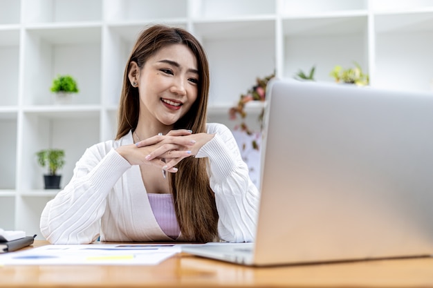 Mooie Aziatische zakenvrouw zit in haar privékantoor, ze praat met haar partner via videogesprek op haar laptop, ze is een vrouwelijke directeur van een startend bedrijf. Concept van financieel beheer