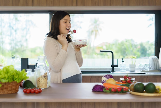 Mooie Aziatische zwangere vrouw eet met lust granen bij het ontbijt in de keuken thuis