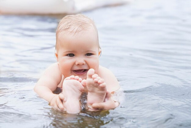 mooie baby baadt in het water en houdt zijn benen vast