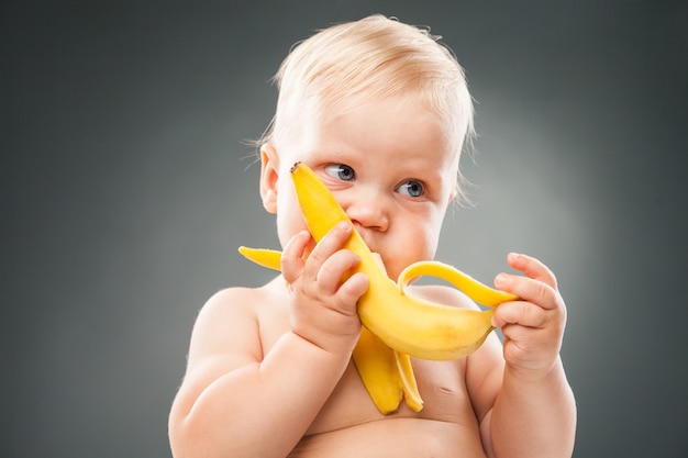 Mooie baby die banaan eet over grijze achtergrond