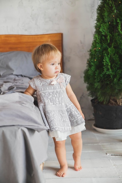 Mooie baby in jurk staande in de slaapkamer bij het bed