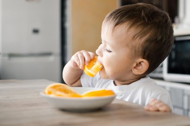 Mooie babyjongen in de keuken die gretig een sinaasappel eet, in partjes gesneden