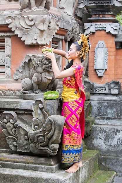 Mooie Balinese vrouw die traditionele kleren draagt en offers legt op een gebeeldhouwd standbeeld in een tempel