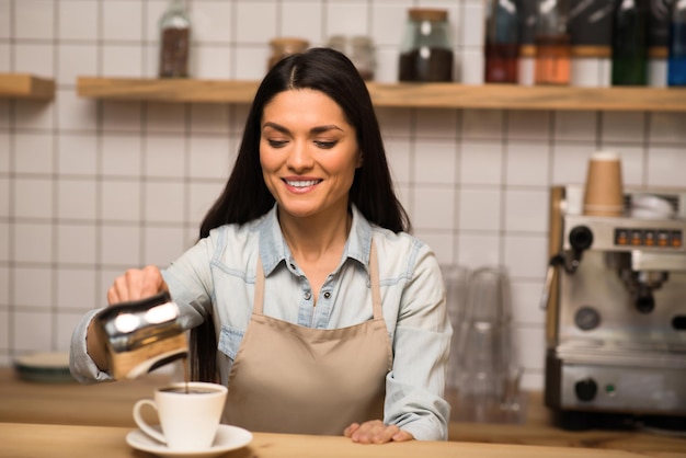 Mooie barista die koffie in de kop giet