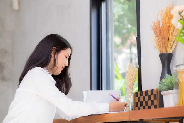 Mooie bedrijfs Aziatische jonge vrouw die op notitieboekje op lijst schrijft.