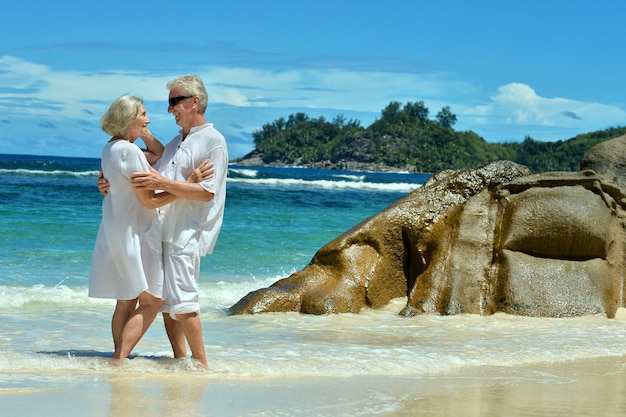 Mooie bejaarde echtpaar staande op het strand omarmen
