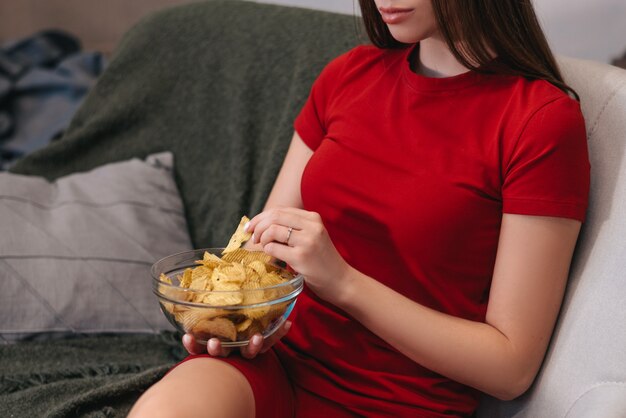 Mooie binnenlandse meisje chips eten, tv kijken, zittend op de bank.