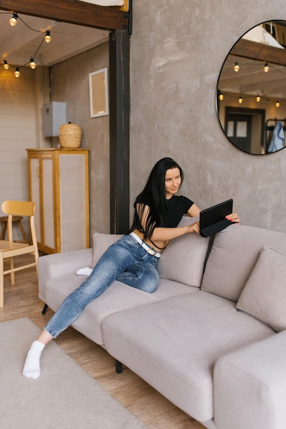 Mooie blanke brunette gekleed in een zwart T-shirt zit op de bank in de woonkamer