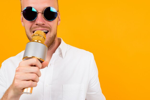 Mooie blanke man met bril zingt liedjes in karaoke met microfoon geïsoleerd op geel