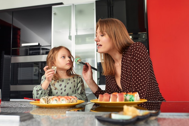 Mooie blanke moeder en dochter die broodjes en sushi eten tijdens de familielunch thuis Bezorgvoedsel Traditioneel Japans eten