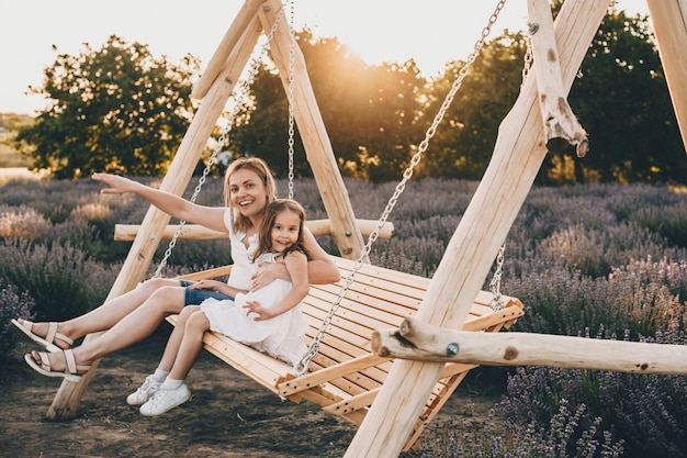 Mooie blanke moeder en haar kleine dochter zitten in een schommel met een lavendelveld op de achtergrond